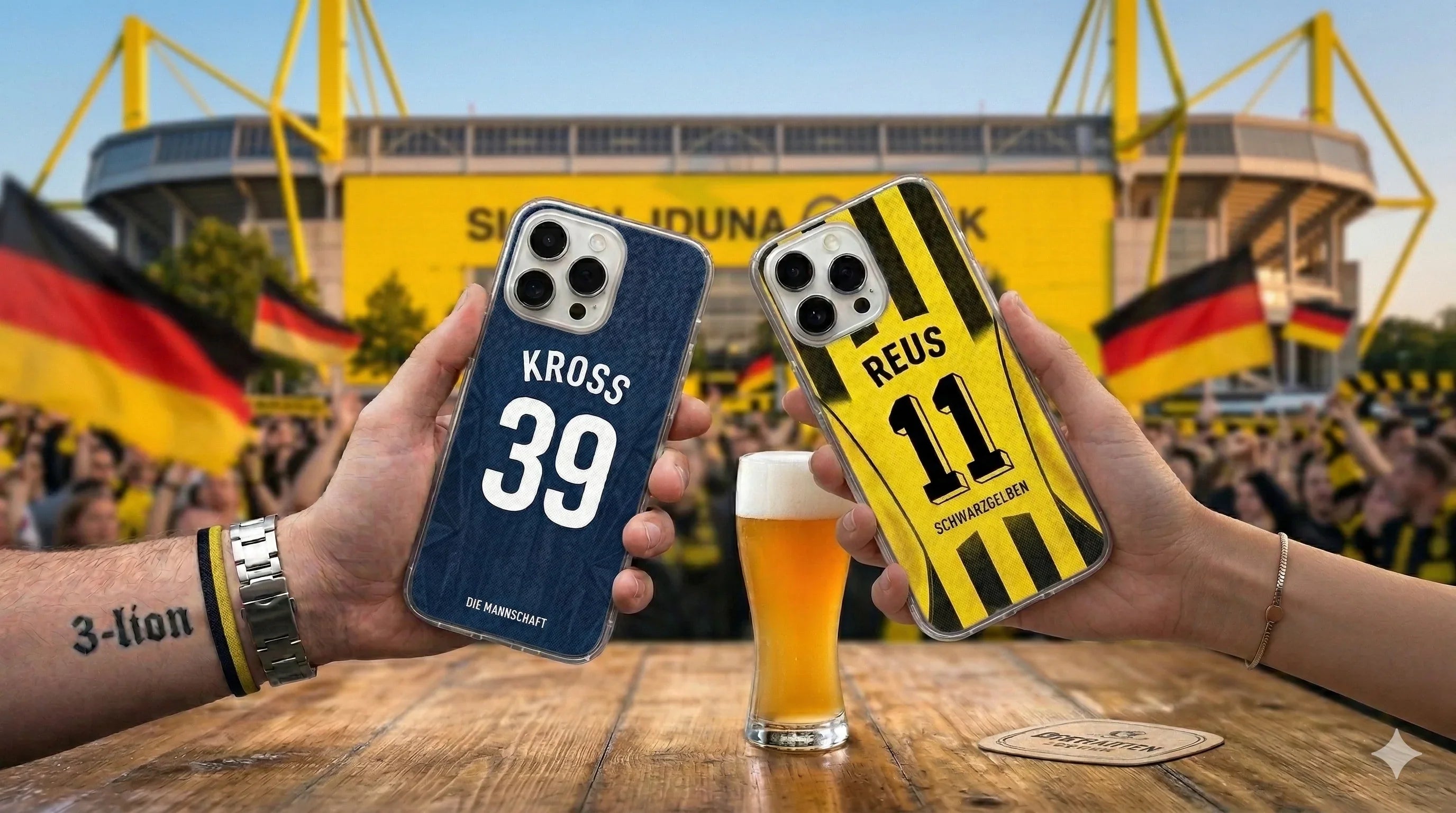 First-person view of hands holding two custom phone cases with "KROSS 39" and "REUS 11" designs over a wooden table with a beer. The background features a blurred, vibrant Dortmund stadium filled with cheering fans and German flags