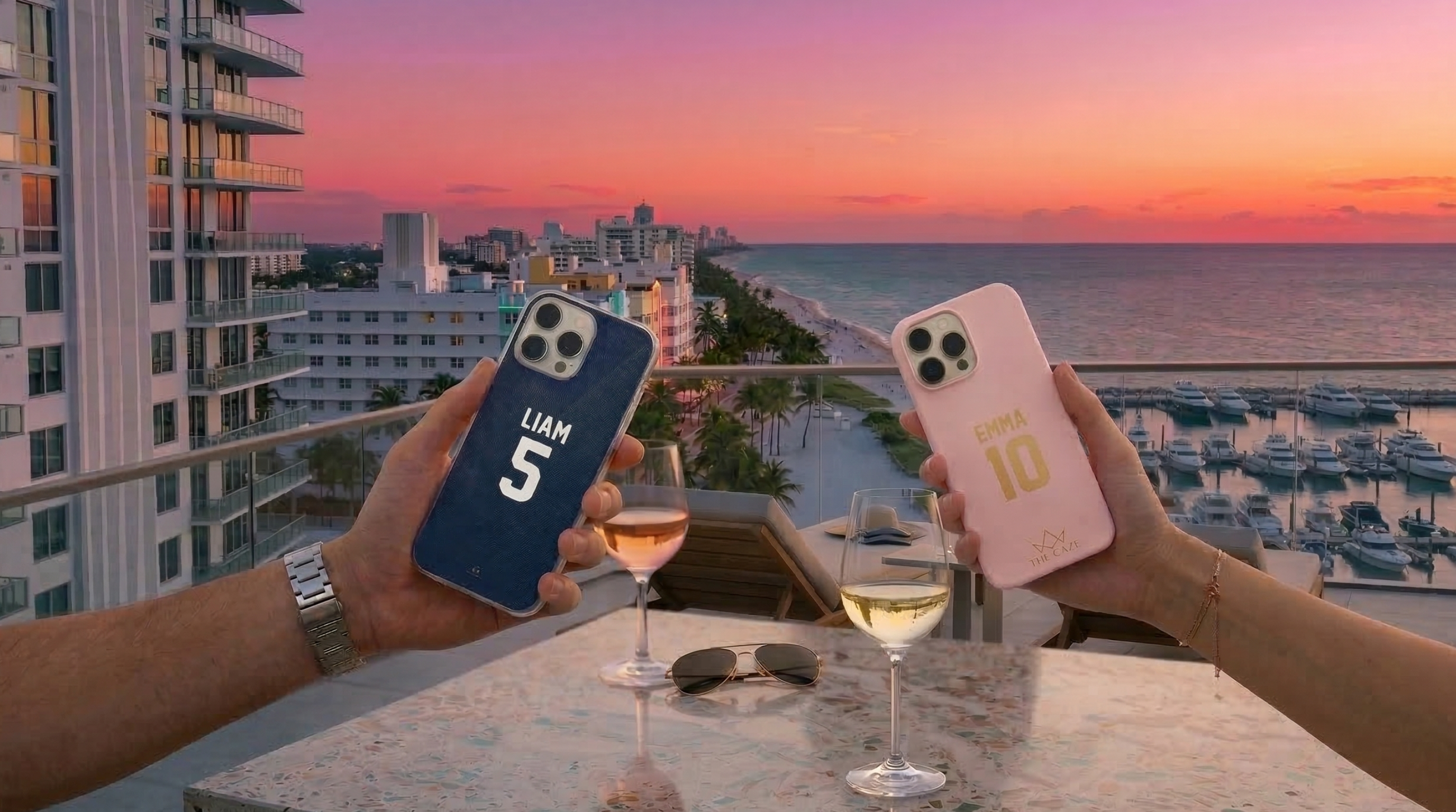 Personalized couple phone cases inspired by football jerseys, held on a rooftop overlooking the ocean at sunset.